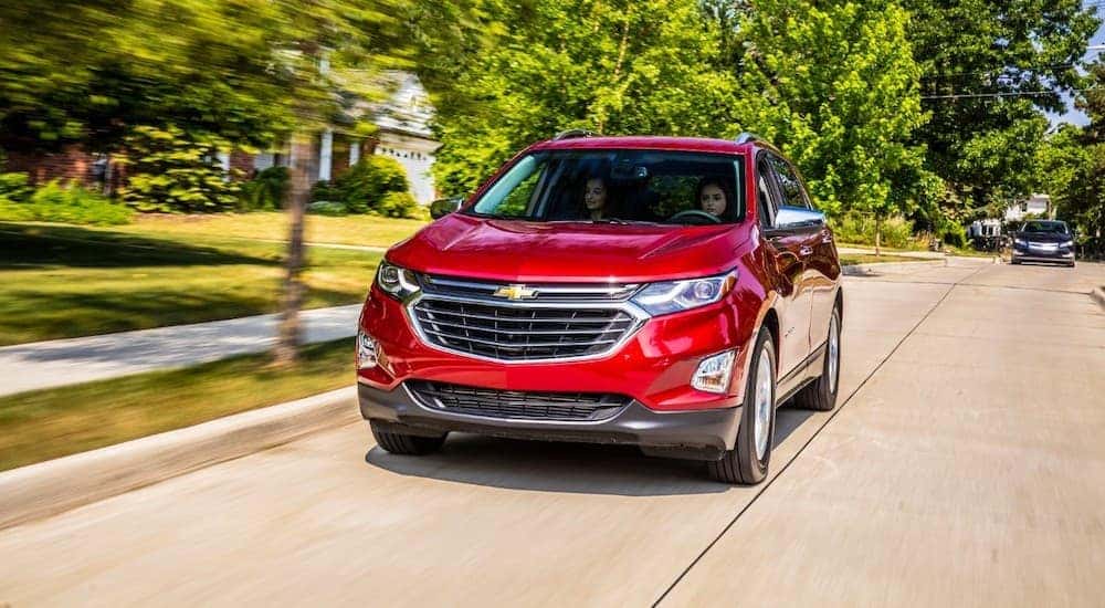A red 2018 Chevy Equinox is shown driving through the suburbs after leaving a certified pre-owned Chevrolet dealer.