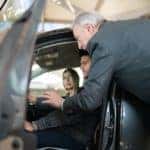 A salesperson is showing a couple the inside of a car at a Certified Pre-Owned GMC dealer.