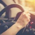 A person is shown driving a car in close up.