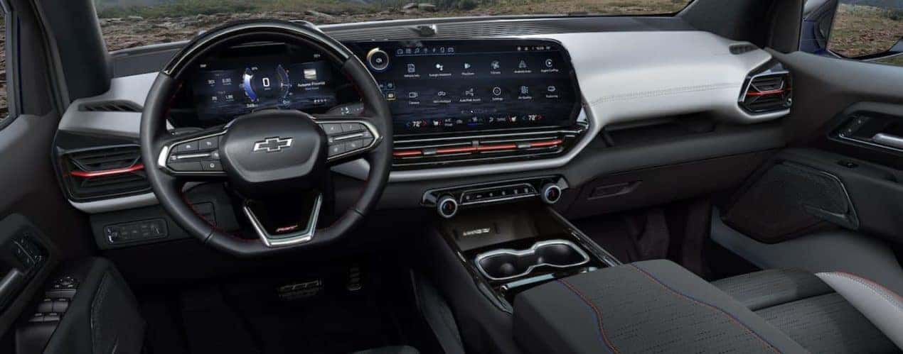 The black interior of a 2024 Chevy Silverado EV shows the steering wheel and infotainment screen.