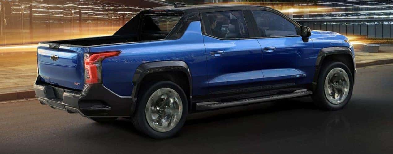 A blue 2024 Chevy Silverado EV is shown from the side driving on an open road during a 2024 Chevy Silverado EV vs 2022 Ford F-150 Lightning comparison.