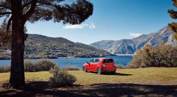 A red 2018 Chevy Sonic LT is shown from the rear near a lake and mountains.