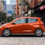 An orange 2021 Chevy Spark is shown from the side driving on a city street.