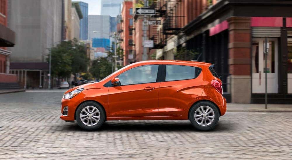 An orange 2021 Chevy Spark is shown from the side driving on a city street.
