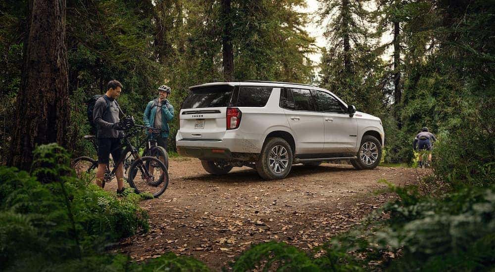 A white 2021 Chevy Tahoe is shown parked in the woods next to people biking.