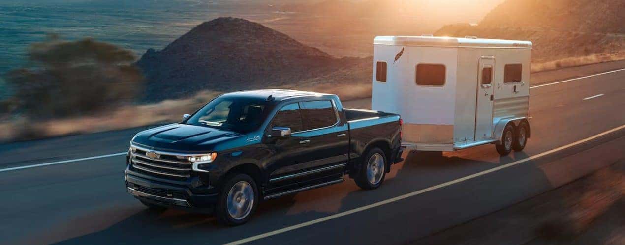 A black 2022 Chevy Silverado High Country is shown towing a horse trailer.