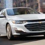 A white 2022 Chevy Malibu is shown driving though a city.