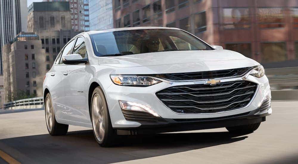 A white 2022 Chevy Malibu is shown driving though a city.