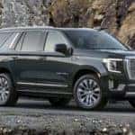 A black 2022 GMC Yukon denali is shown from the side parked in front of a mountain.