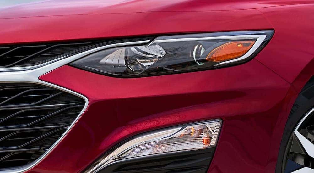 A close up shows the driver side headlight on a red 2022 Chevy Malibu.