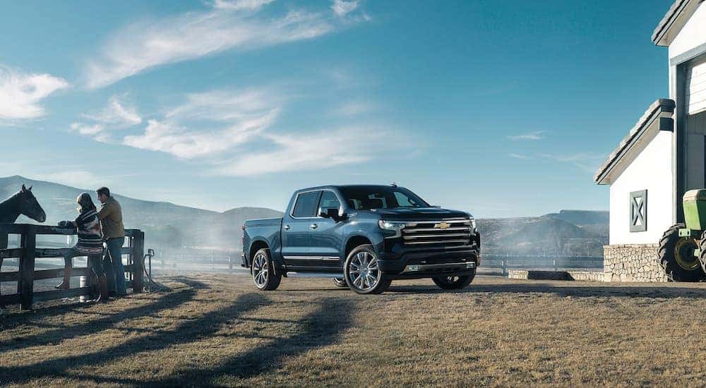 A blue 2022 Chevy Silverado 1500 High Country is shown parked on a farm.