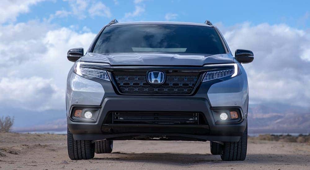 A silver 2021 Honda Passport Elite is shown from the front parked on a sandy lot.