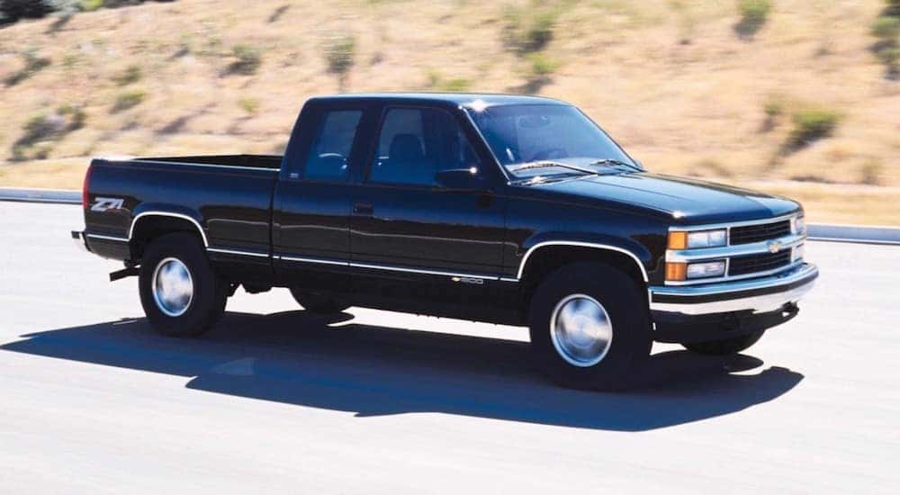 A black 1999 Chevy Silverado Z71 is shown from the side while driving down the road after leaving a dealership that sells used Chevy trucks.