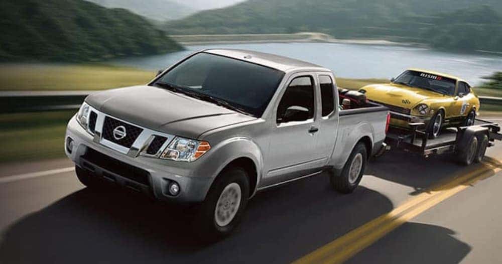 A silver 2019 Nissan Frontier is shown towing a yellow car on a highway.