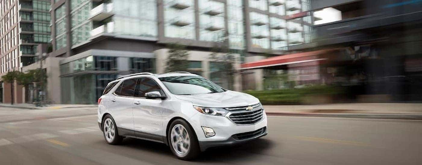 A white 2018 Chevy Equinox is shown driving on a city street to check out a certified Chevrolet for sale.