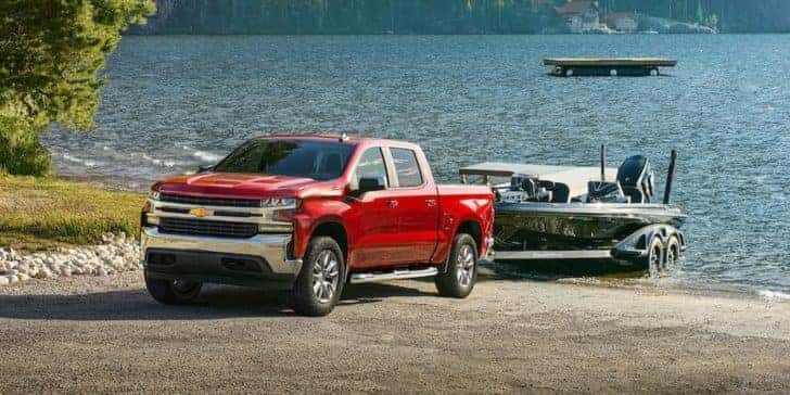 A red 2022 Chevy Silverado 1500 is shown towing a boat out of a lake.