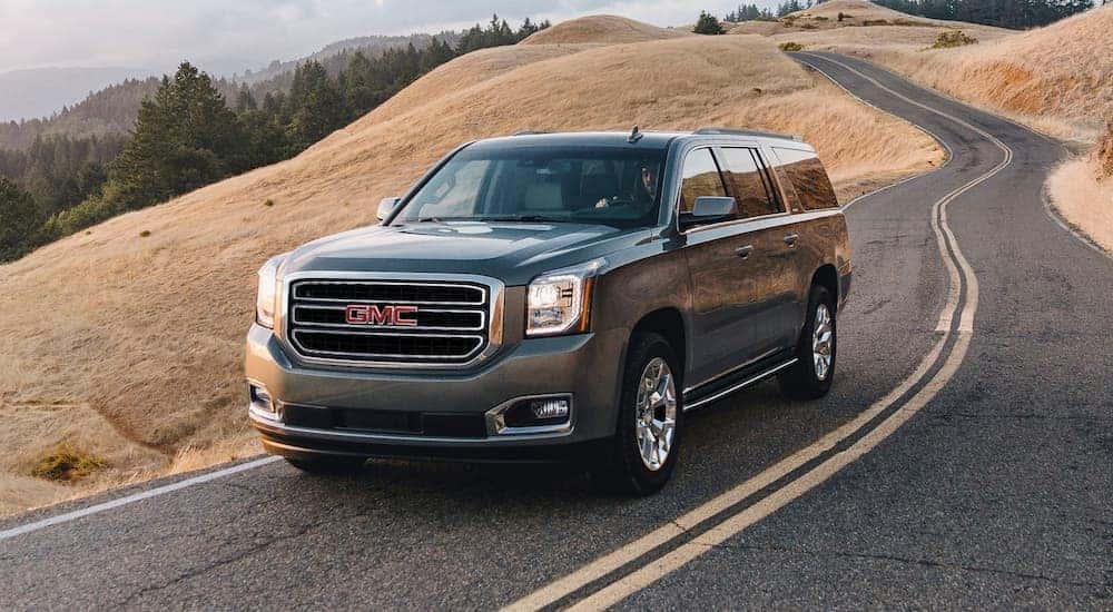 A popular certified GMC for sale, a grey 2020 GMC Yukon, is shown from the side on an open road.