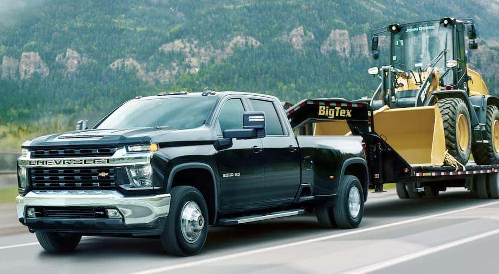 A black 2021 Chevy Silverado 3500HD is shown towing heavy machinery on a trailer.