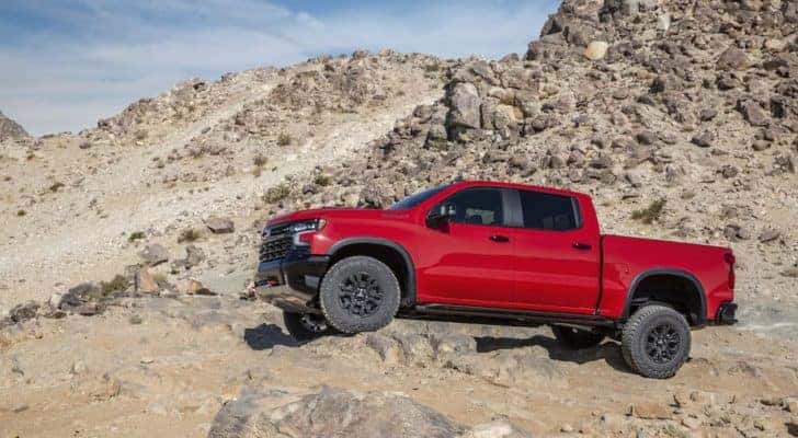 A red 2022 Chevy Silverado ZR2 is shown from the side while driving off-road.