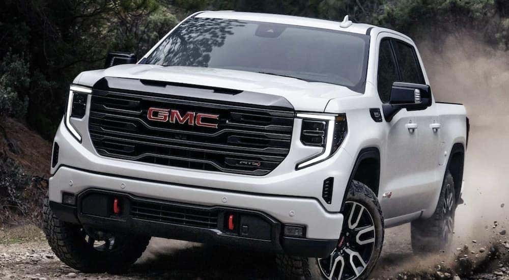 A white 2023 GMC Sierra 1500 AT4 kicking up dirt as it drives up a mountain