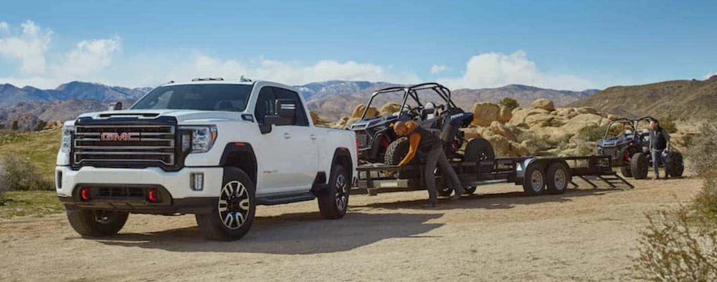 A white 2020 GMC Sierra 2500 AT4 is shown from the front while towing a UTV.