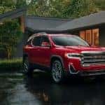 A red 2023 GMC Acadia parked outside of a modern home with large windows