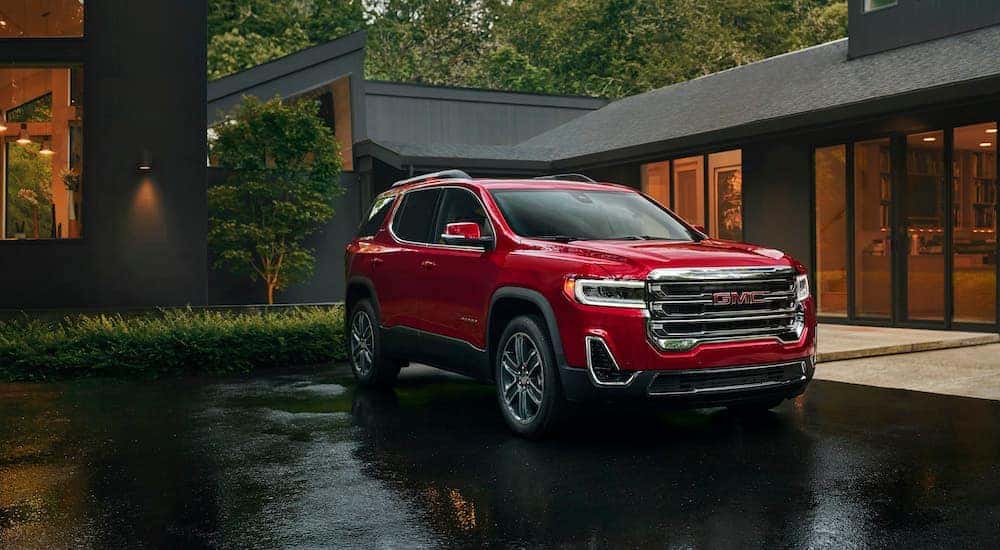 A red 2023 GMC Acadia parked outside of a modern home with large windows