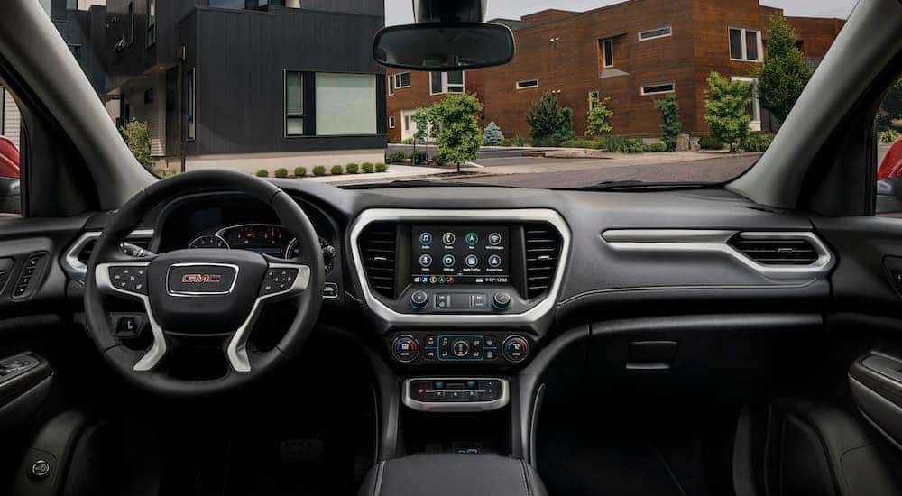 The black and silver interior of a 2023 GMC Acadia with modern buildings seen through the windows