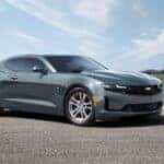 A grey 2023 Chevy Camaro parked in an open lot surrounded by fields