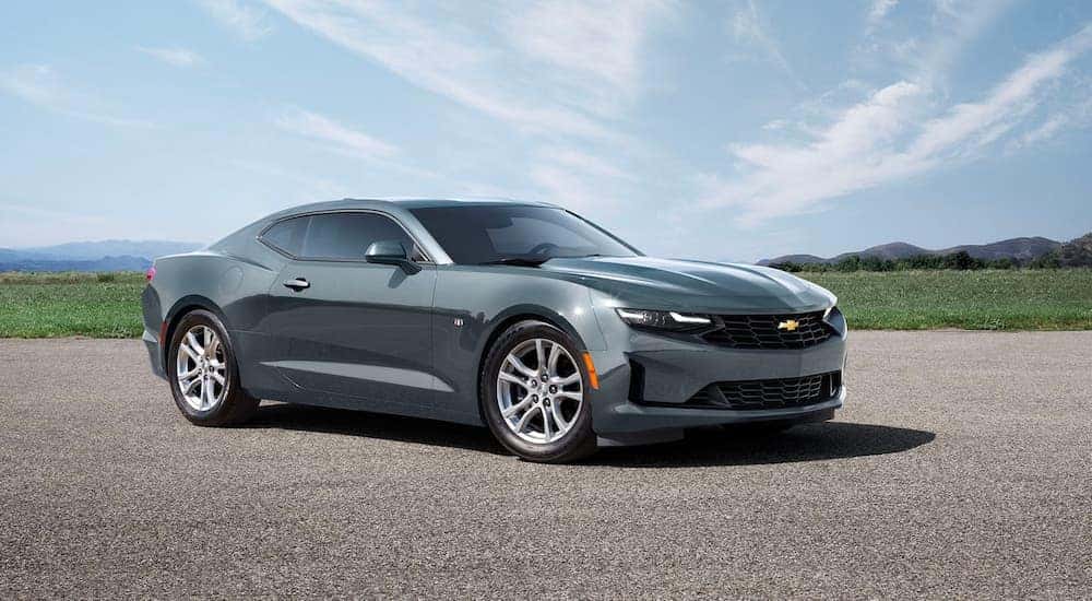 A grey 2023 Chevy Camaro parked in an open lot surrounded by fields