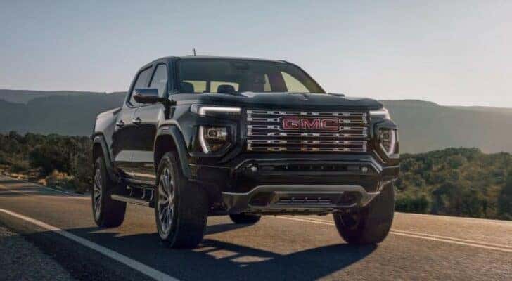 A popular GMC truck for sale, a black 2023 GMC Canyon Denali, is shown driving on an open road.