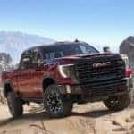 A red 2024 GMC Sierra 2500HD AT4X is shown parked on rocks in a desert.