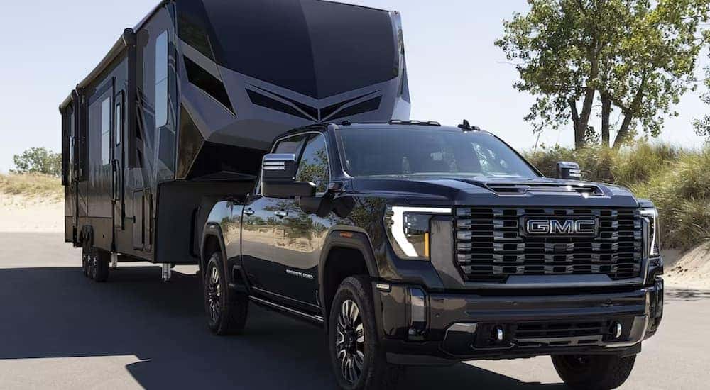 A black 2024 GMC Sierra 2500 HD Denali Ultimate is shown towing a large camper trailer.