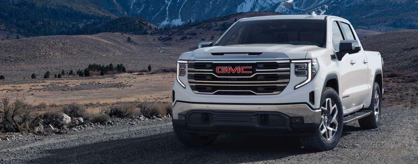 A popular Sierra for sale, a white 2023 GMC Sierra 1500, is shown driving on a trail.
