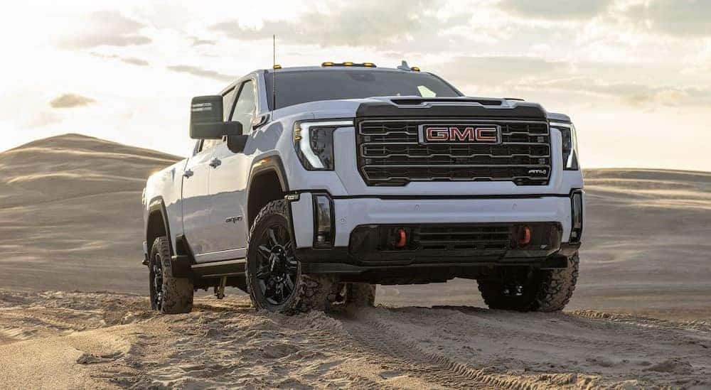 A white 2024 GMC Sierra 2500 HD AT4 is shown parked off-road on sand.
