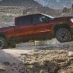 A red 2024 GMC Sierra 3500 HD AT4X is shown driving off-road after visiting a GMC Sierra for sale.