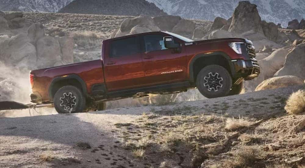 A red 2024 GMC Sierra 3500 HD AT4X is shown driving off-road after visiting a GMC Sierra for sale.