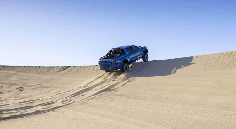 A blue 2023 Chevy Colorado ZR2 is shown from the rear at an angle while driving off of a sand dune.