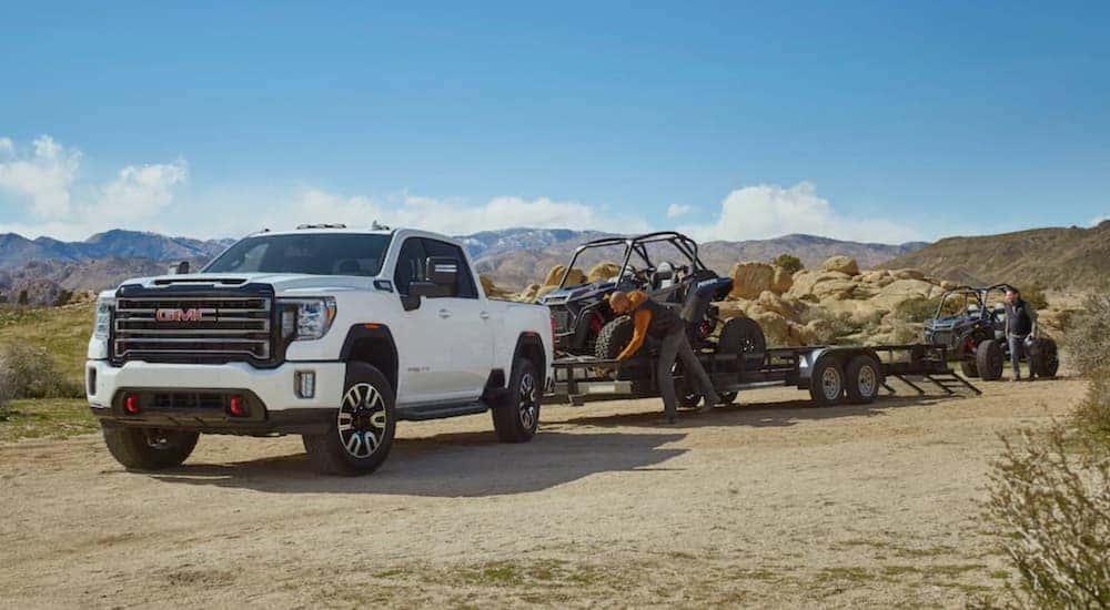 A white 2020 GMC Sierra 2500 HD AT4 is shown from the front at an angle while towing a UTV.