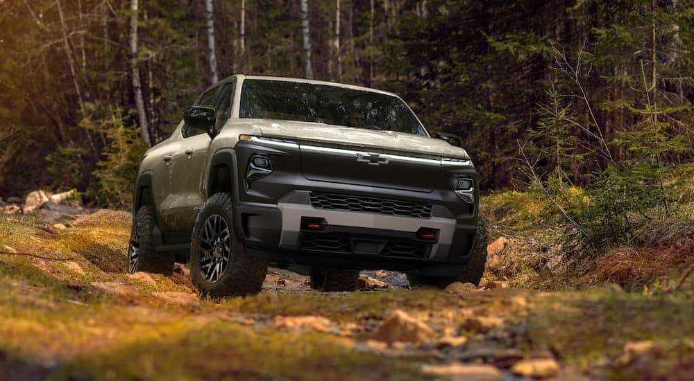 A tan 2024 Chevy Silverado EV Trail Boss is shown from the front while off-road after leaving a dealer that has Chevy trucks for sale.