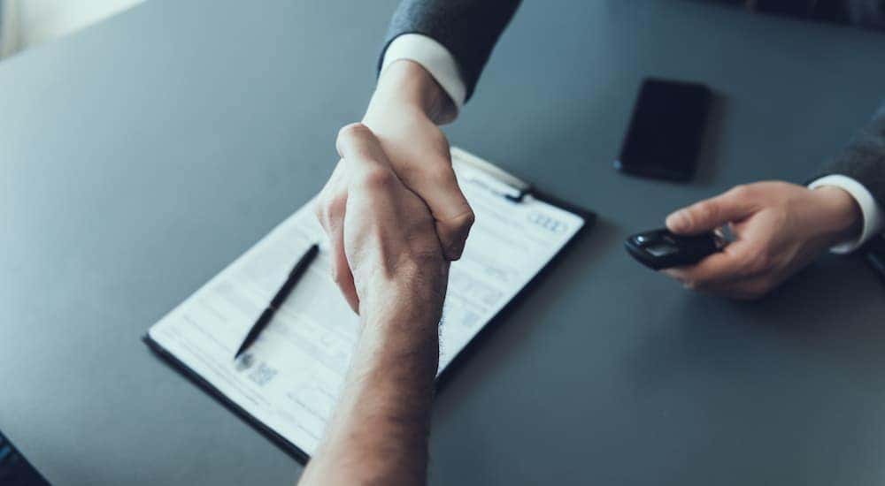 Two people are shown shaking hands over paperwork regarding how to "sell my car".