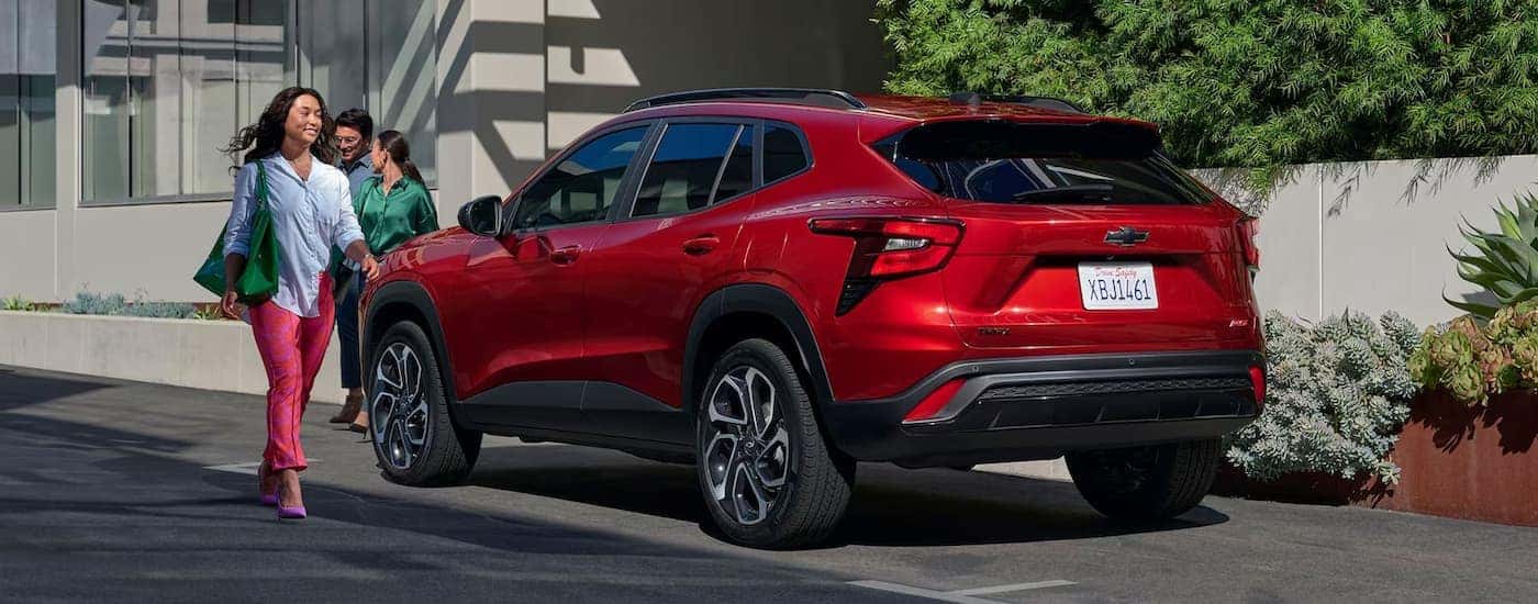 A red 2024 Chevy Trax is shown from the side parked on the side of a city street.