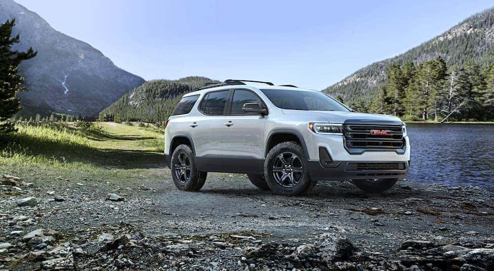 A white 2024 GMC Acadia AT4 is shown parked near a lake.