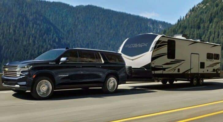 A blue 2023 Chevy Suburban High Country is shown towing a trailer after visiting a Fayetteville Chevy dealer.