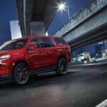 A red 2024 Chevy Tahoe is shown driving on a city street after visiting a Fayetteville Chevy Dealer.