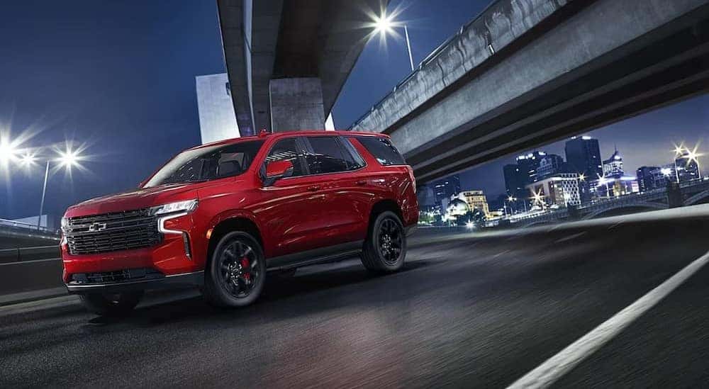 A red 2024 Chevy Tahoe is shown driving on a city street after visiting a Fayetteville Chevy Dealer.
