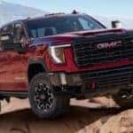 A red 2024 GMC Sierra 2500 HD is shown driving off-road.