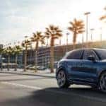 2019 Porsche Cayenne driving on palm tree lined road near stadium