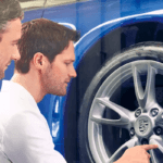Service advisor and customer examining wheel on blue Porsche on lift