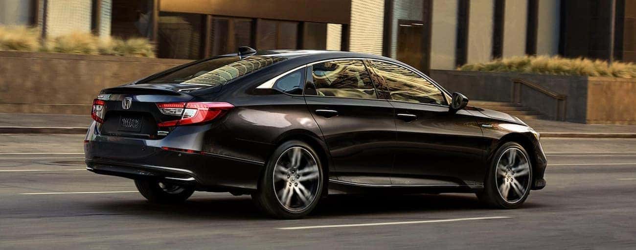 A black 2021 Honda Accord Hybrid is driving on a city street after winning the 2021 Honda Accord vs 2021 Kia K5 comparison.
